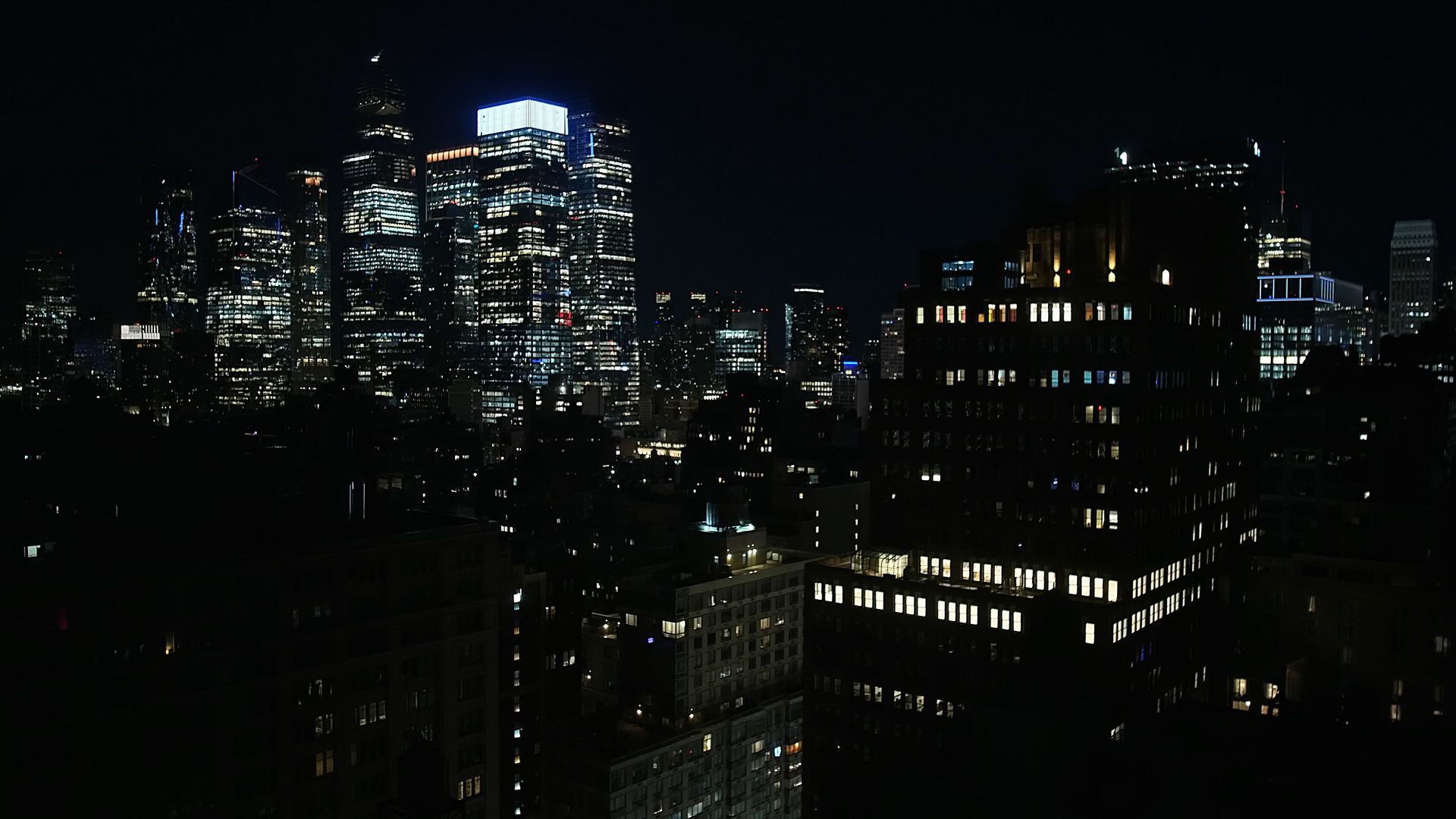 New York City at night in clear weather: stacked lit office windows across dark towers under a black sky.