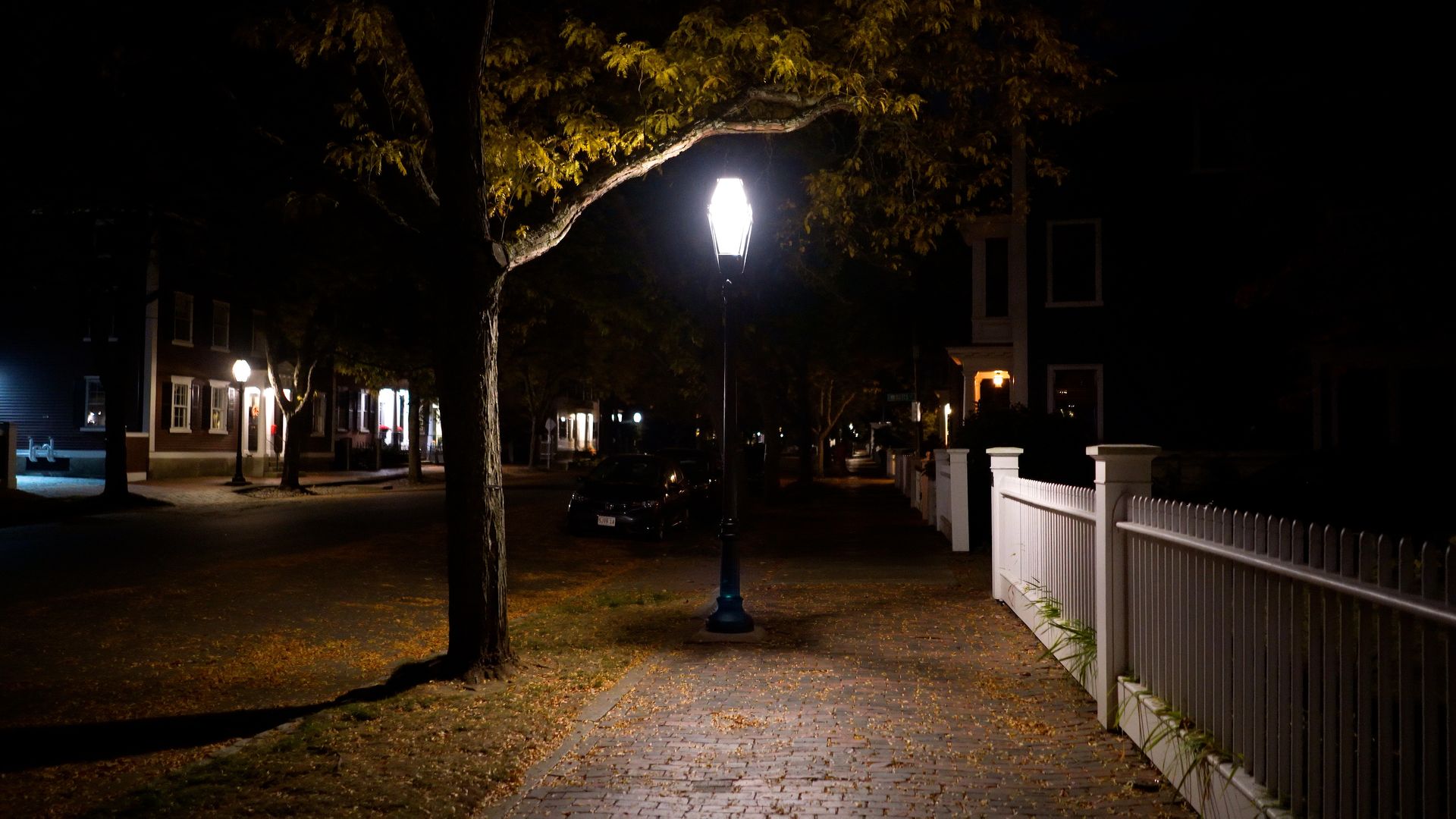 Salem at 2 AM in the dark: a lantern-style lamppost lit above a brick sidewalk scattered with fallen leaves