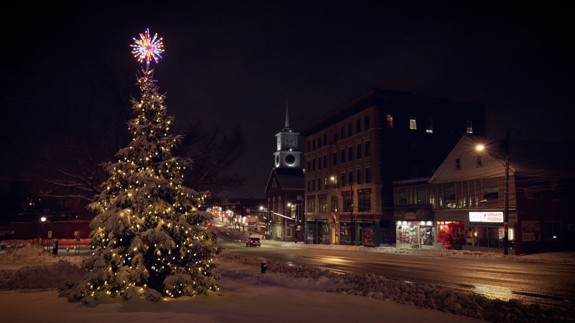 A lit Christmas tree in a small New England town square during a night snowstorm