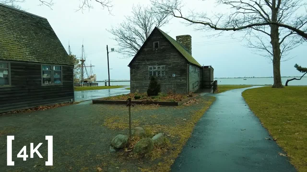 Plymouth, Massachusetts at morning in rain: a wet path past weathered wooden buildings, with ship masts and the bay beyond.