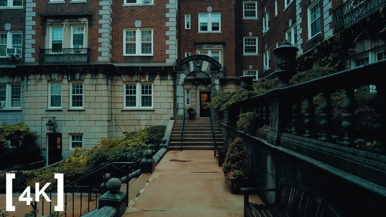 Harvard neighborhood, Cambridge on a gray day in rain: stone steps and a balustrade rising to a brick apartment archway with one lit doorway.