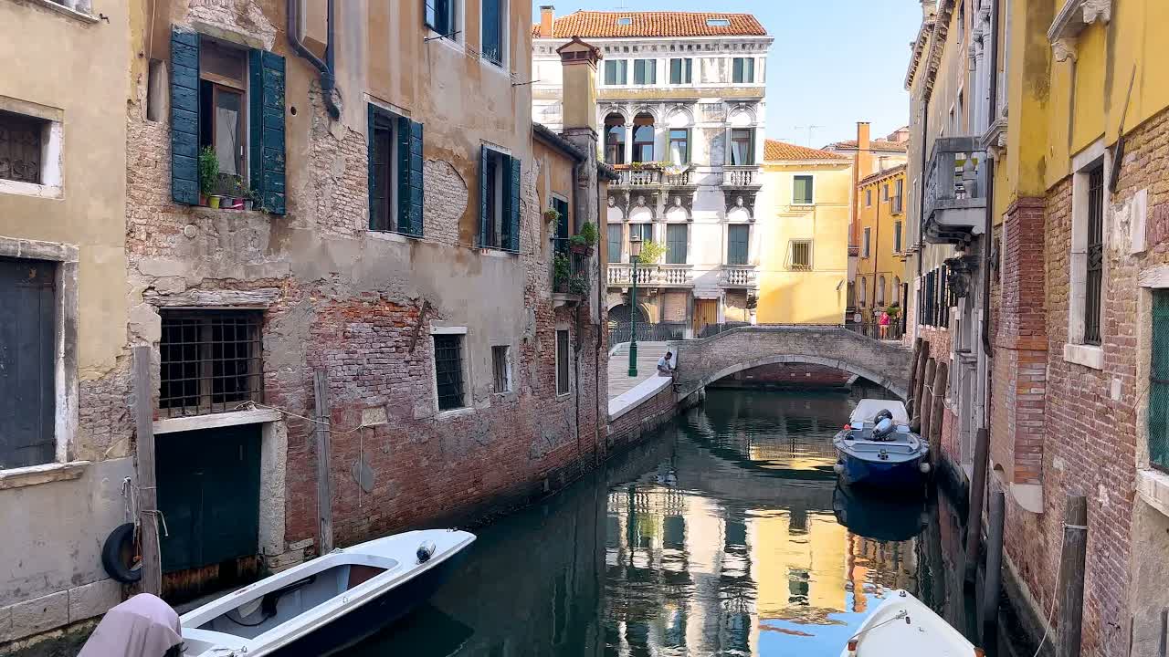 Venice at daytime in sunlight: motorboats moored on green canal water beneath a small stone footbridge