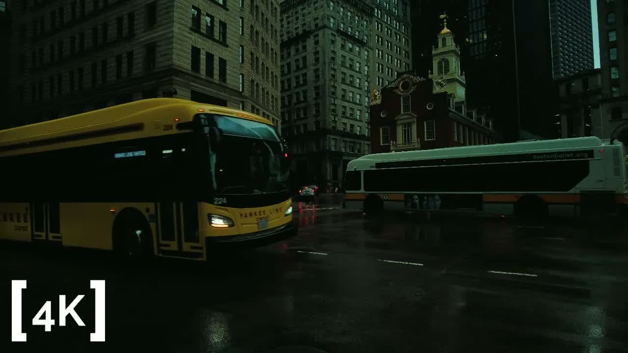 Downtown Boston at morning in rain: the Old State House tower rising behind two buses crossing a wet intersection