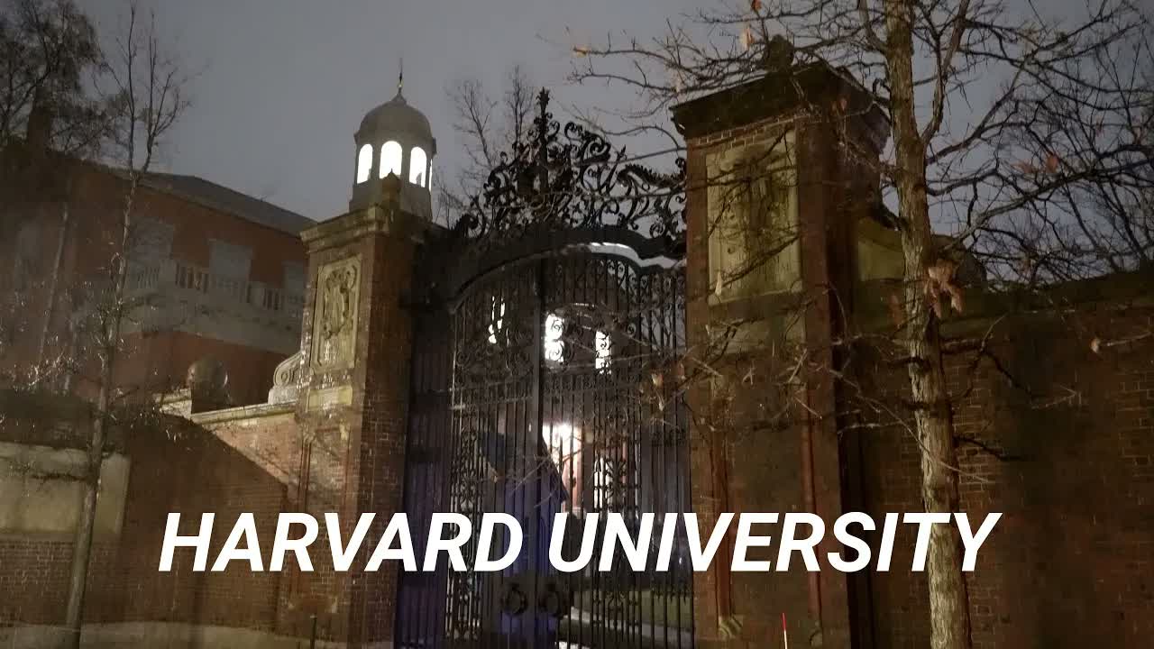 Harvard Yard, Cambridge at night in rain: a lit cupola lantern above wrought-iron gates hung between brick piers.