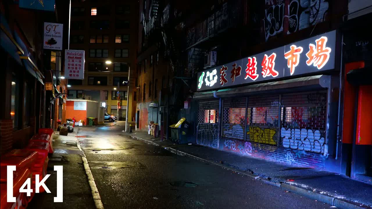 Downtown Boston at night in rain: a lit market sign in Chinese characters above graffiti-covered shutters in a narrow street.