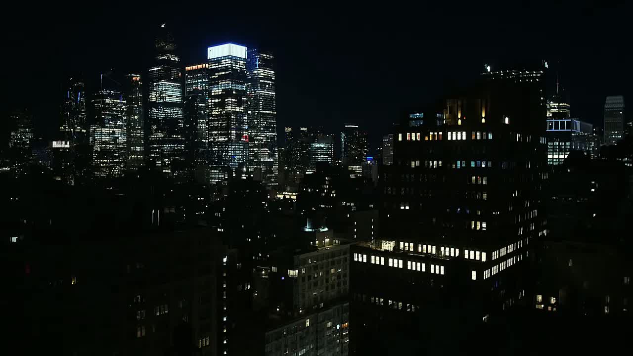 New York City at night in clear weather: stacked lit office windows across dark towers under a black sky.