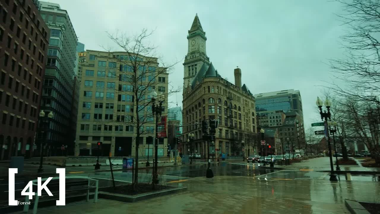 Downtown Boston at morning in rain: a stone clock tower rising over a rain-slicked, nearly empty plaza