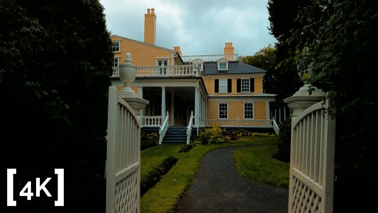 Cambridge at daytime in rain: a yellow clapboard house with white porch railings seen through an open white wooden gate