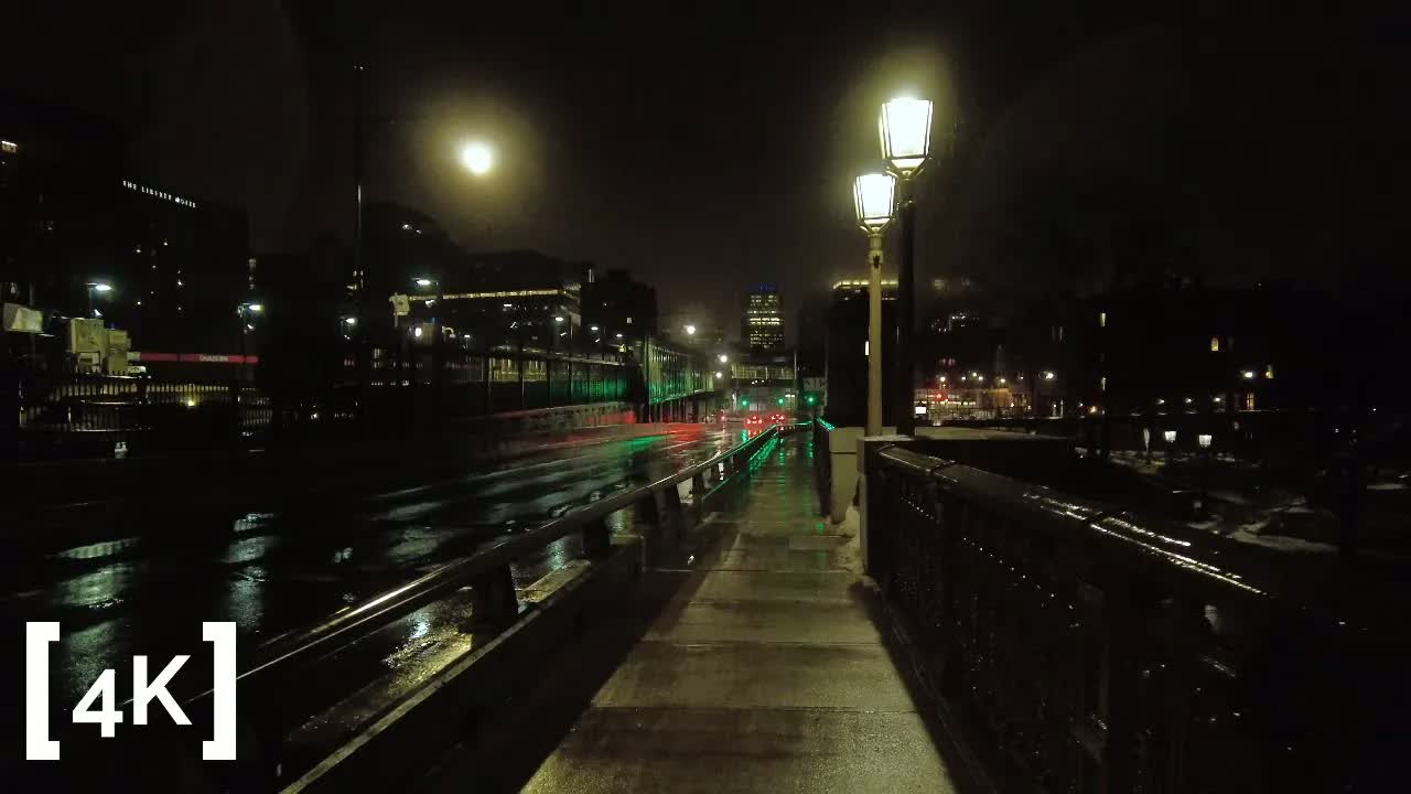 Longfellow Bridge, Boston at night in rain: twin lamps glowing over a wet sidewalk, signal lights streaking the roadway.