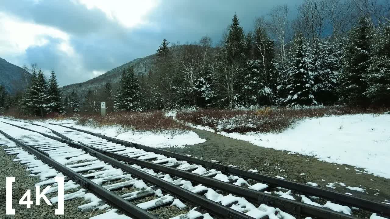 New England mountains at daylight in snow: snow-dusted railroad tracks branching below white-capped evergreens.