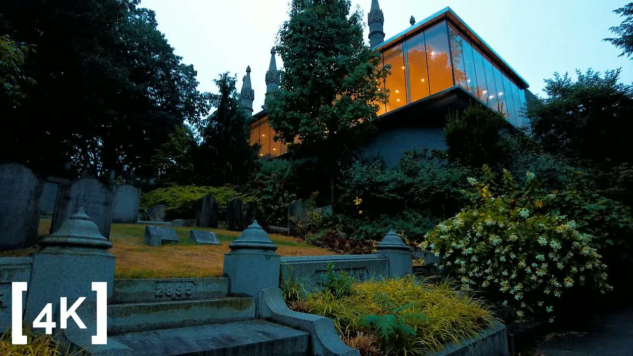 Auburn Cemetery at evening before a rainstorm: headstones on a sloped lawn below a lit glass building
