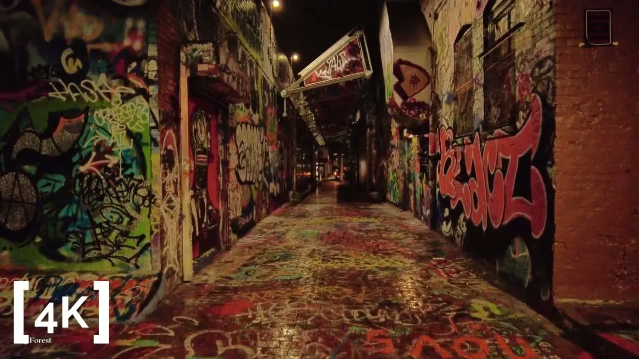 Cambridge at midnight in rain: a graffiti-covered alley with wet painted brick shining under lamplight