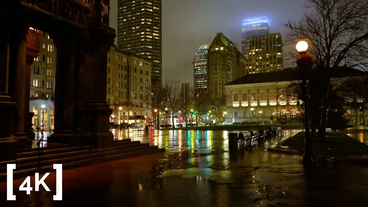 Copley Square, Boston at night in rain: streetlight and tower light reflecting in long streaks across the wet plaza by the library.