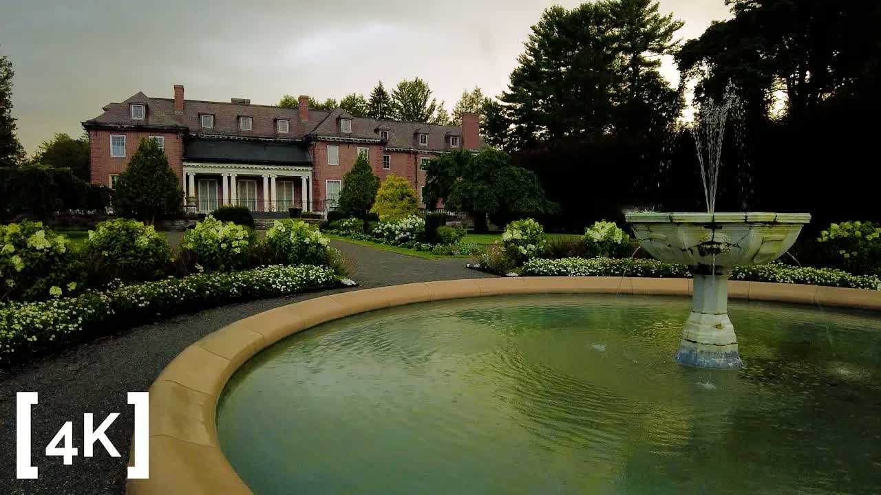 A garden outside Boston at the end of summer in heavy rain: rain stippling a stone fountain's pool in front of a brick manor house.