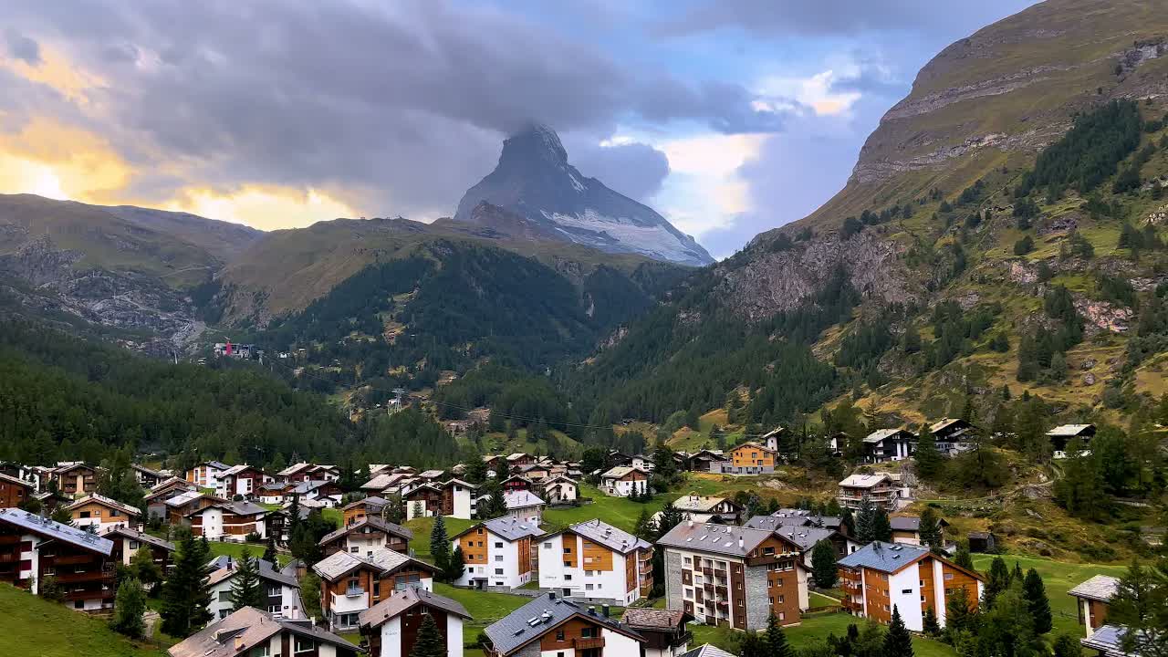 Zermatt, Switzerland on a summer day: village chalets in the valley below the Matterhorn, its peak wrapped in cloud.