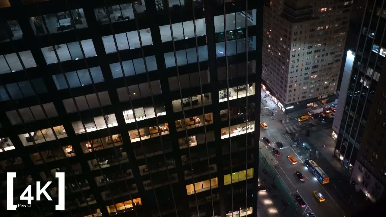 Midtown Manhattan at late night from a high open window: lit office towers and yellow cabs on the avenue below