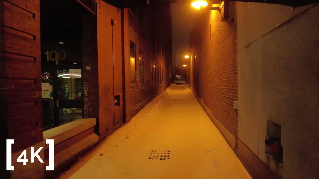 A New England mill town at evening in freezing rain: fresh footprints in a snow-dusted alley between brick mill walls.