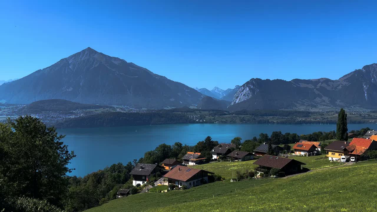 Sigriswil, Switzerland at daytime in clear weather: village rooftops on a green slope above a blue lake, with peaks behind