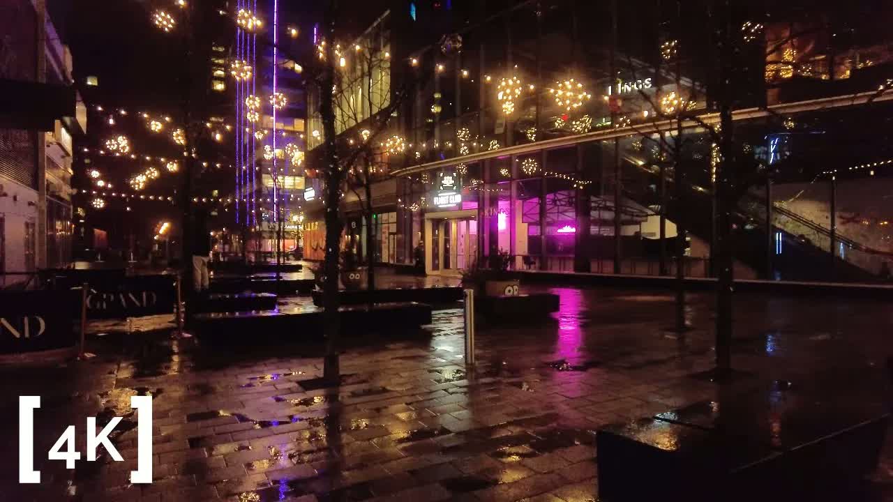 Boston Seaport at midnight in rain: strings of globe lights over an empty plaza, pink storefront glow pooling in the puddles.