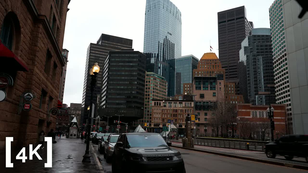 Boston's Financial District in daylight after heavy rain: a lit lamppost over a wet brick sidewalk, glass towers rising behind.