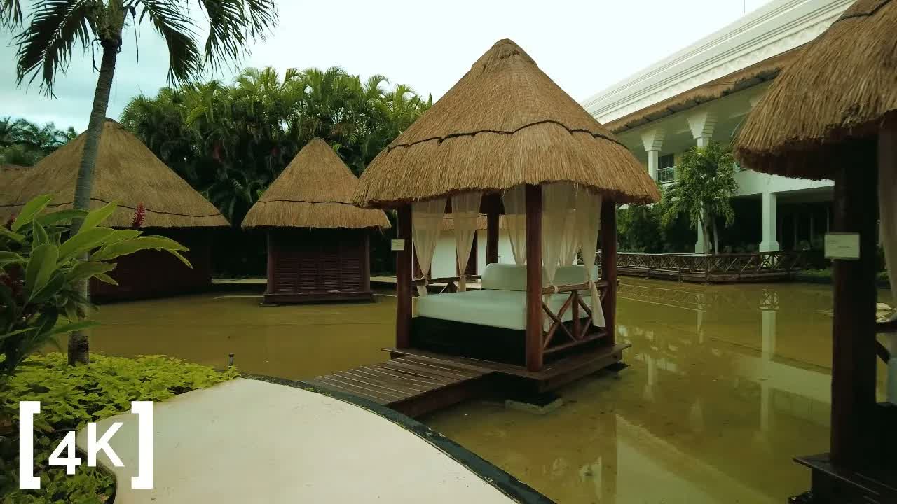 A Riviera Maya resort, Mexico at sunrise in morning light: thatched-roof cabanas standing in a shallow reflecting pool among palms.