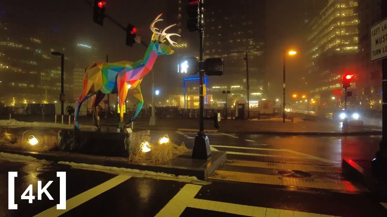 Boston Seaport at night in fog: a multicolored geometric deer sculpture standing over a wet crosswalk.