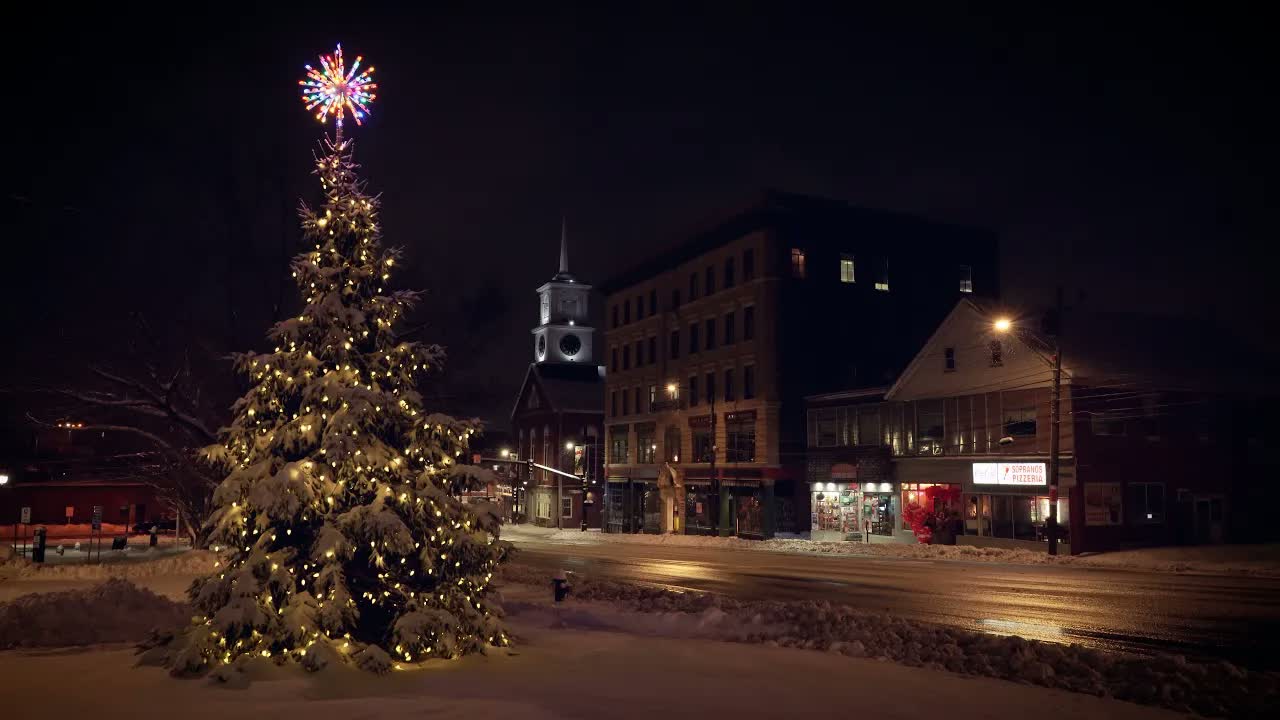 Snow falling on a lit Christmas tree in a quiet New England town square at night