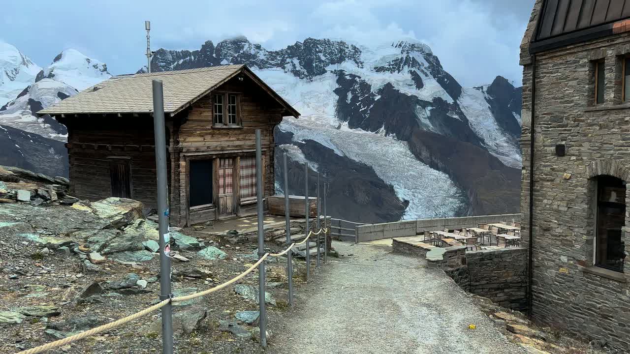 Gornergrat summit at daytime under storm clouds: a wooden hut on the rocky ridge above the Gorner Glacier