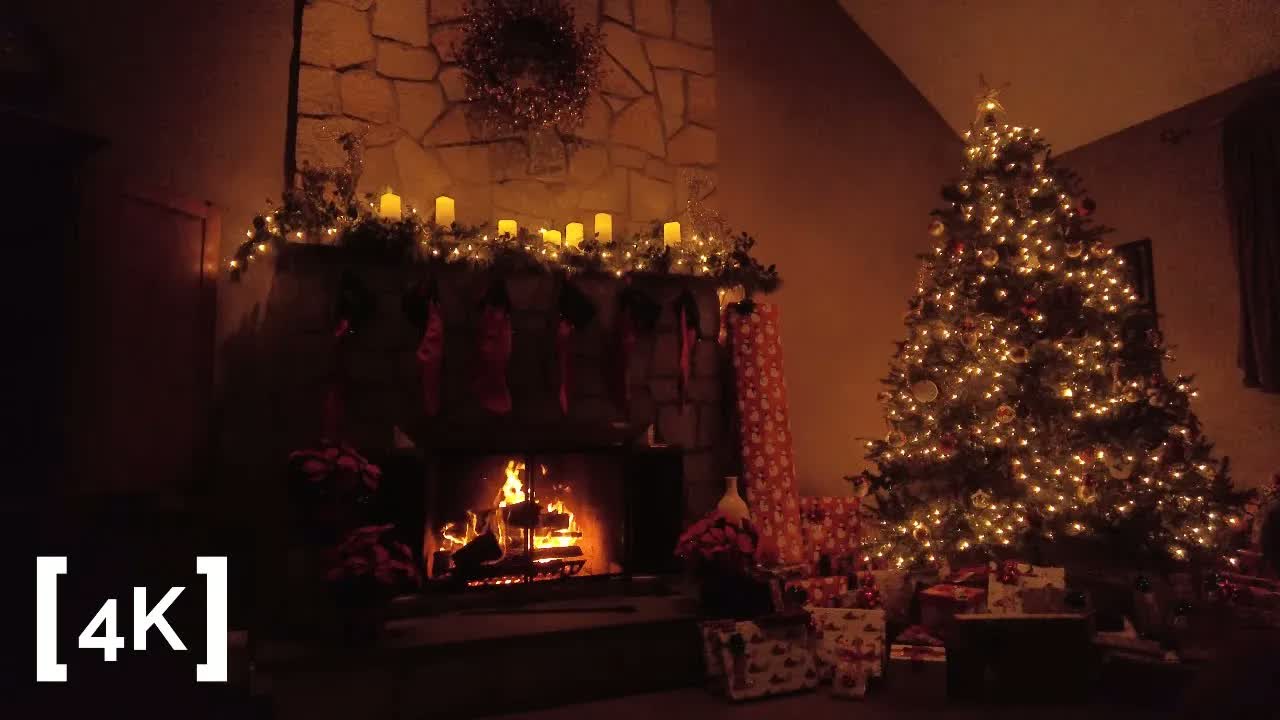 A stone fireplace at night in winter: stockings and lit candles on the mantel beside a Christmas tree strung with lights.